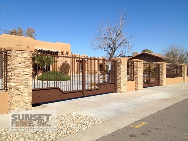 A gated driveway with a metal fence and stone wall.